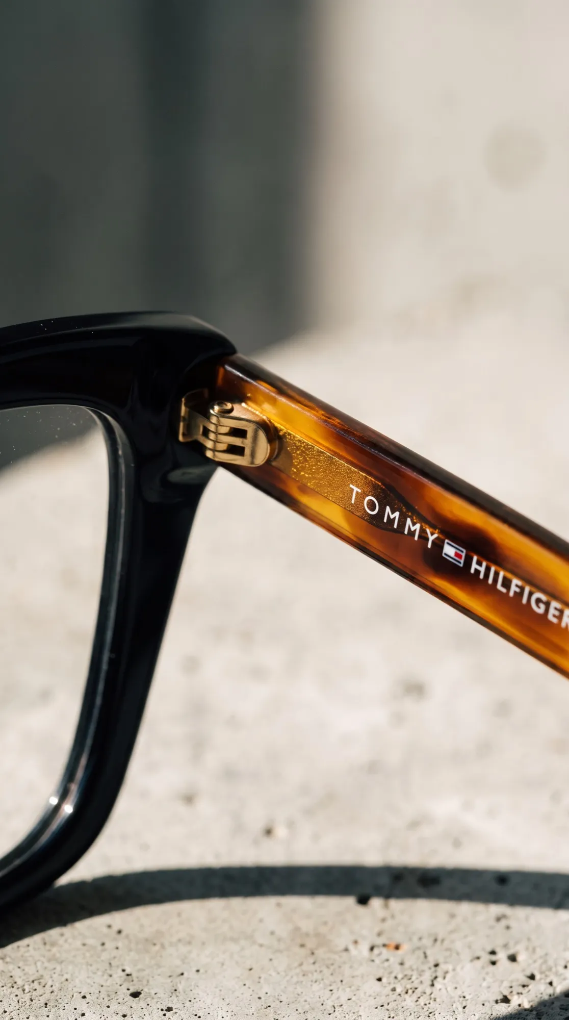 Detalhe da haste de uma armação Tommy Hilfiger, com a dobradiça dourada em close